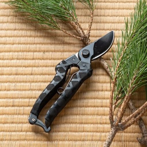 YH-1 Black Masamune pruning shears placed on a traditional Japanese tatami mat, next to pine branches